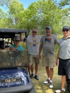 Three men and two young boys standing around a golf cart smiling for a picture.