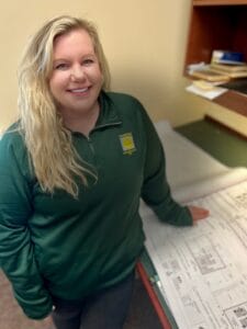 Young woman with long blonde curly hair standing with construction plans on the table beneath her.