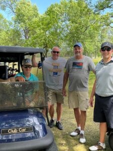 Three men and two young boys standing around a golf cart smiling for a picture.