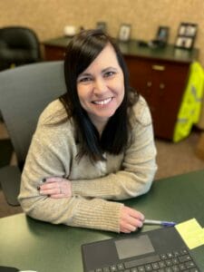 Woman with long dark hair and hazel eyes smiling for a candid picture at her desk.