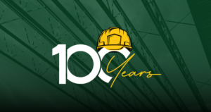 100-year logo with yellow hard hat icon and background image in green overlay of metal beams at a construction jobsite. Our 100-year theme is Building our Communities since 1924, one vision at a time.