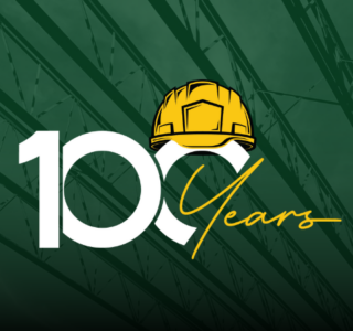 100-year logo with yellow hard hat icon and background image in green overlay of metal beams at a construction jobsite. Our 100-year theme is Building our Communities since 1924, one vision at a time.