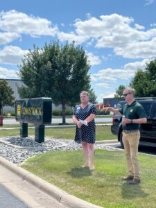 Michael Comstock stands on grassy boulevard next to Bradley Aune from the FMWF Chamber of Commerce, giving a talk about the history of Comstock Construction.
