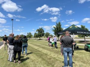 About ten people standing on grass with tent in background and blue sky with clouds.