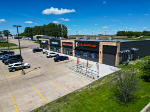 Exterior aerial view of a newly constructed strip mall with black brick and light wood paneling accents.