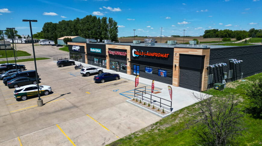 Exterior aerial view of a newly constructed strip mall with black brick and light wood paneling accents.