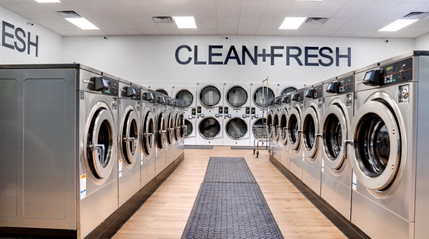 Looking down aisle of washing machines on each side with a row of double stacked machine on the back wall.