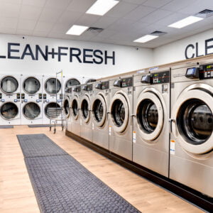 Looking down aisle of washing machines on each side with a row of double stacked machine on the back wall.