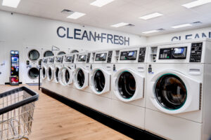 Row of white laundry machines with the words "Clean+Fresh" on the back white wall.