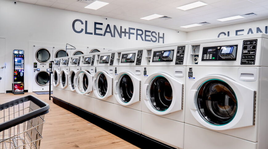 Row of white laundry machines with the words "Clean+Fresh" on the back white wall.