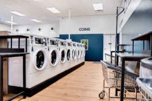 Row of white washing machines with storage bins to the right side.