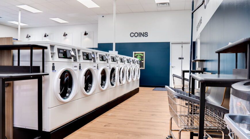 Row of white washing machines with storage bins to the right side.