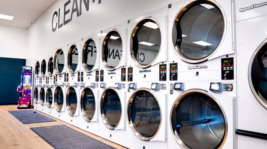 Double stacked row of white dryers lining the wall at laundromat.