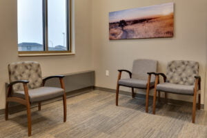 Waiting room with three chairs, bright double window and artwork of country fields on the wall.