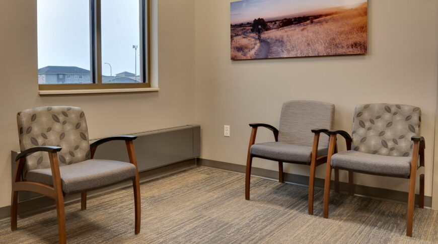 Waiting room with three chairs, bright double window and artwork of country fields on the wall.