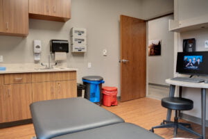 Physical therapy clinic examination room with faux-wood laminate flooring and greige walls.