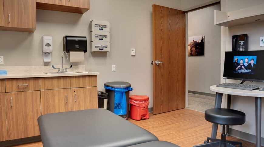 Physical therapy clinic examination room with faux-wood laminate flooring and greige walls.