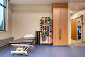 Adjustment table with resistance weights and bands stacked in open shelving to the right of the bed. Enclosed floor to ceiling cabinetry next to it on the far right.