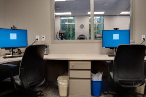 Physical therapy rehab office with see-through window overlooking the therapy gym. Two workstations sharing a back counter with file cabinetry in between.