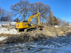 Yellow excavator moving rocks along a riverbank during wintertime.