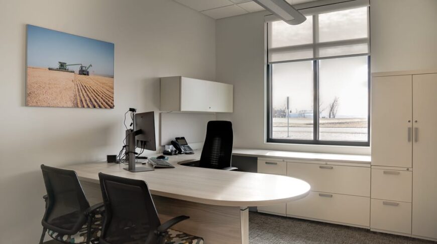 Newly built office with light beige walls, neutral light carpet, light cabinetry and bright window behind desk.