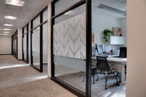 View of office building hallways with floor to ceiling semi-transparent windows glimpsing into modern offices.