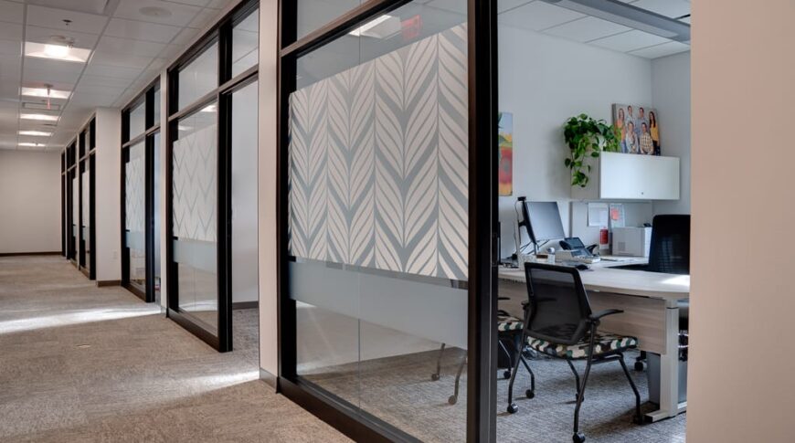 View of office building hallways with floor to ceiling semi-transparent windows glimpsing into modern offices.
