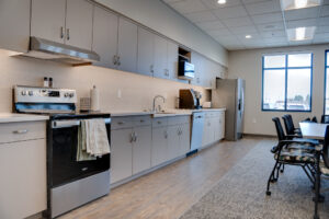 Office community room kitchen that spans the entire length of the back wall, including stove and oven, dishwasher, and fridge.