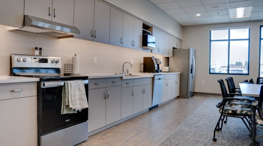Office community room kitchen that spans the entire length of the back wall, including stove and oven, dishwasher, and fridge.