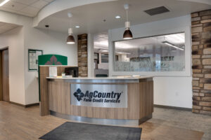 AgCountry Farm Credit Services front reception desk with curved wood laminate and company sign on metal logo over the laminate. Stone columns flank each side of the desk.