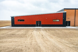 Exterior view of the entrance to the new Selfridge School addition. Bright orange and dark gray building with double doors in the middle and two short, wide windows on either side.