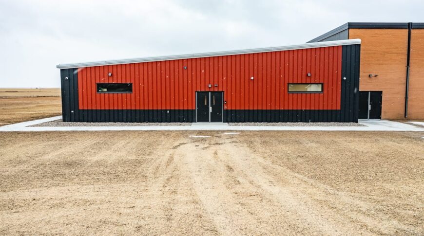 Exterior view of the entrance to the new Selfridge School addition. Bright orange and dark gray building with double doors in the middle and two short, wide windows on either side.