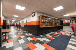 Intersection of two school hallways, one going right, the other left. Bright orange, gray, dark gray, and white accents throughout.