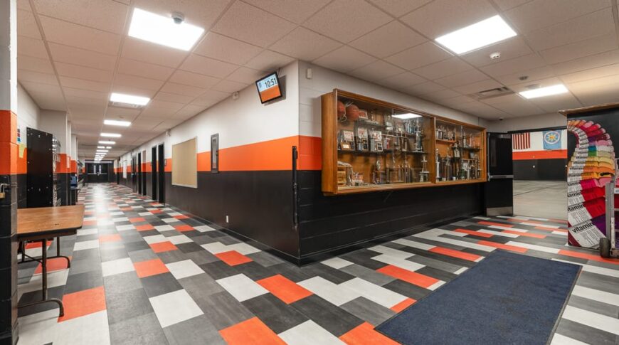 Intersection of two school hallways, one going right, the other left. Bright orange, gray, dark gray, and white accents throughout.
