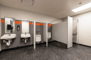 Newly constructed school boys bathroom with gray flooring and gray and white walls with an orange accent band.
