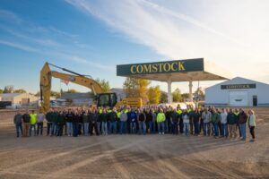 Group picture of the Comstock Construction employees in front of an excavator machine and the Comstock gas pump in the Wahpeton lot.