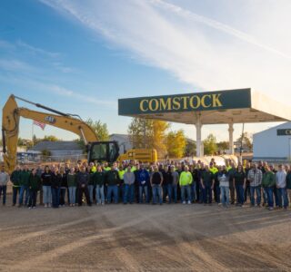 Group picture of the Comstock Construction employees in front of an excavator machine and the Comstock gas pump in the Wahpeton lot.