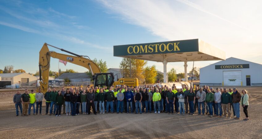 Group picture of the Comstock Construction employees in front of an excavator machine and the Comstock gas pump in the Wahpeton lot.