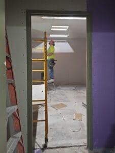 View looking into a room that has a man on drywall stilts working on installing ceiling drywall panels.