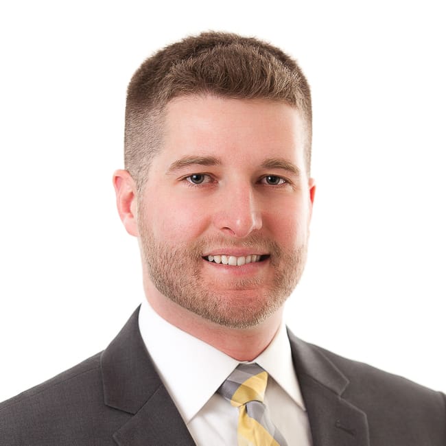 JJohnson_800x800-1 White man with short spiked light brown hair wearing black jacket and white collared shirt with yellow and gray checked tie.