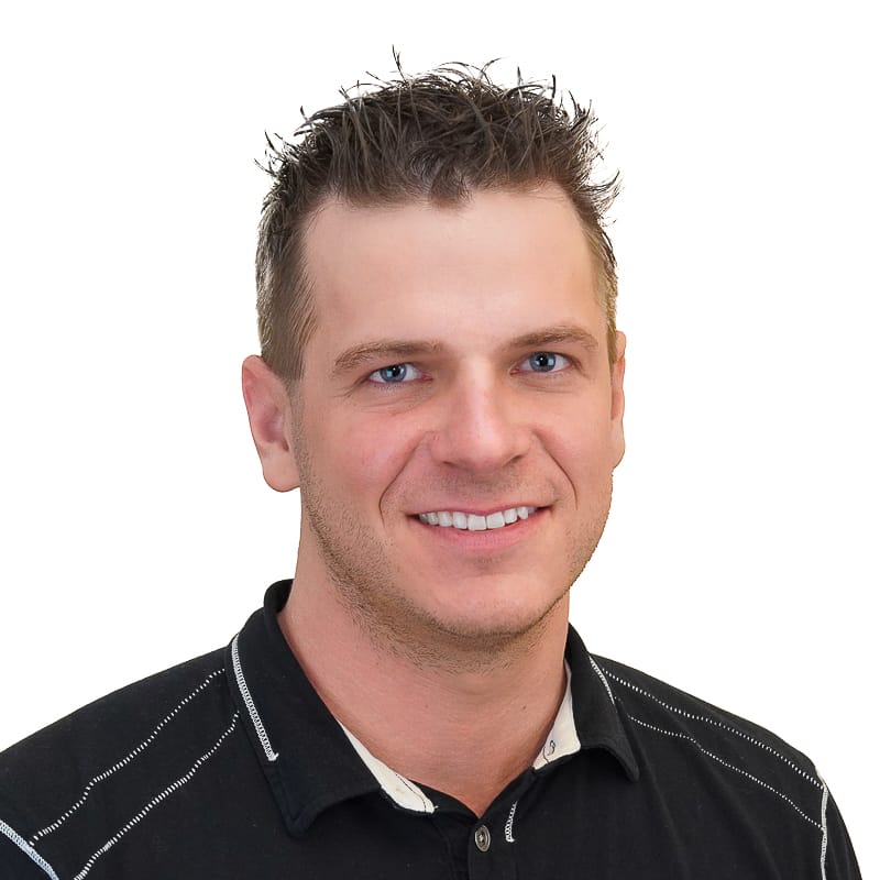 TLies_800x800-1 Young white man with spikey brown hair and blue eyes and black polo smiling on white background.