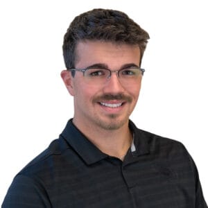 Young man in twenties with short scruffy dark brown hair, brown eyes, and goatee with glasses and black polo striped shirt.