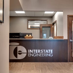 Reception entryway opening to front desk in dark walnut stain with a silver metal sign saying "Interstate Engineering."