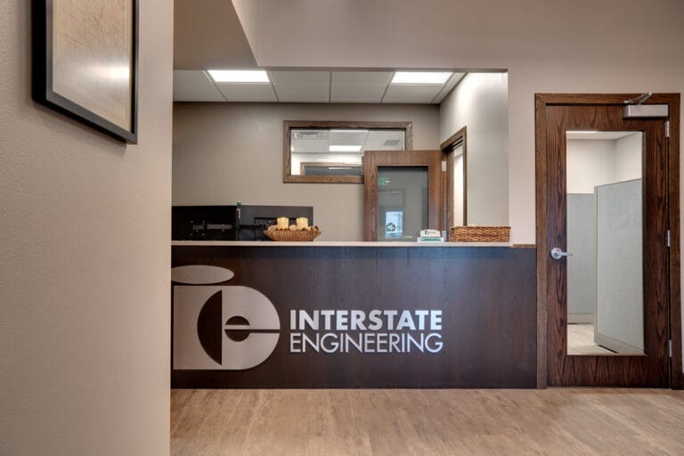 Reception entryway opening to front desk in dark walnut stain with a silver metal sign saying "Interstate Engineering."