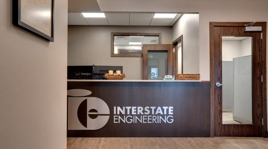 Reception entryway opening to front desk in dark walnut stain with a silver metal sign saying "Interstate Engineering."