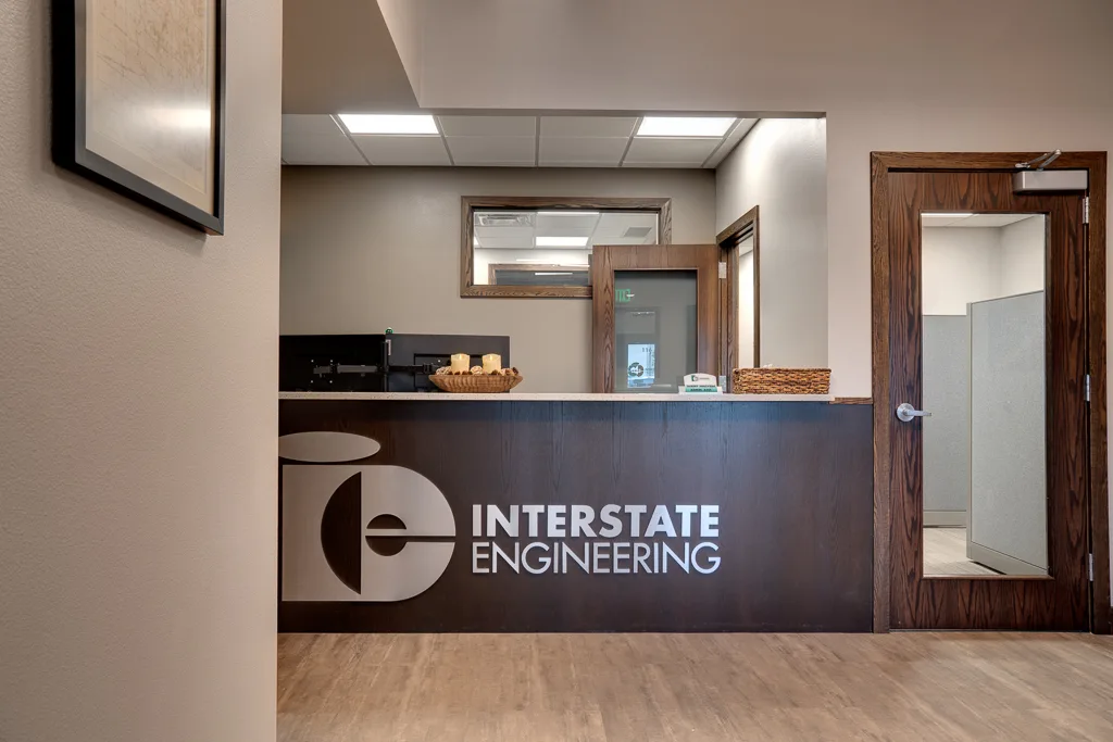 Reception entryway opening to front desk in dark walnut stain with a silver metal sign saying "Interstate Engineering."