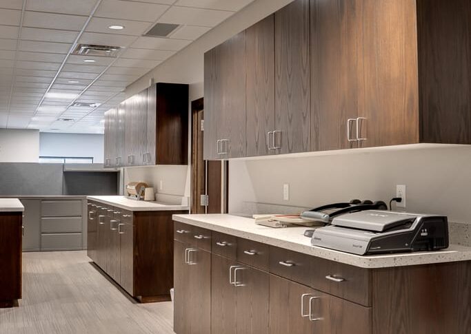 Dark-stained upper and lower cabinetry that is bar-height lined down the office hallway.