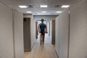 Blue-collar man walking down aisle of tall cubicles.