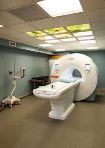 MRI room with MRI machine in the middle and overhead fluorescent lights with treetop visual inserts.