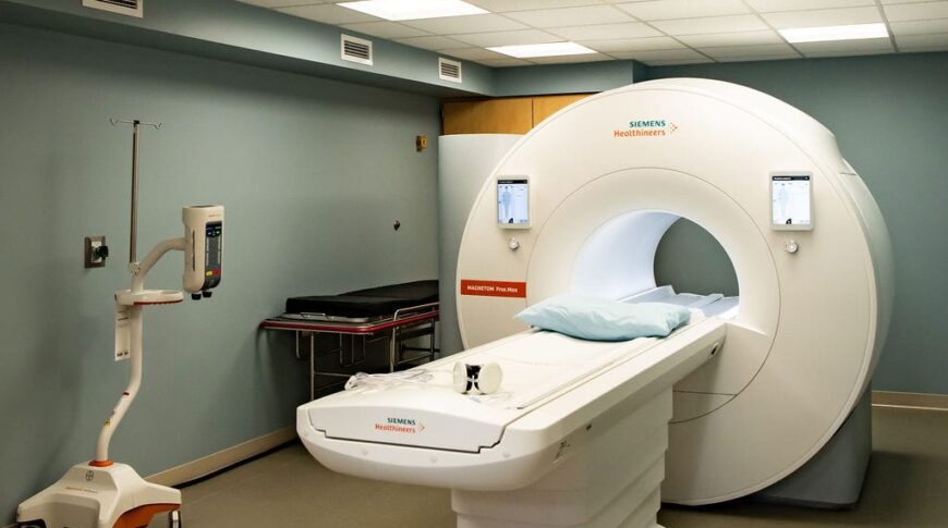 MRI room with MRI machine in the middle and overhead fluorescent lights with treetop visual inserts.